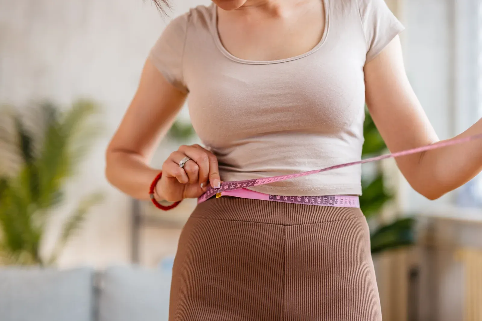 Woman measuring her waist at home to track 12 week personal training results