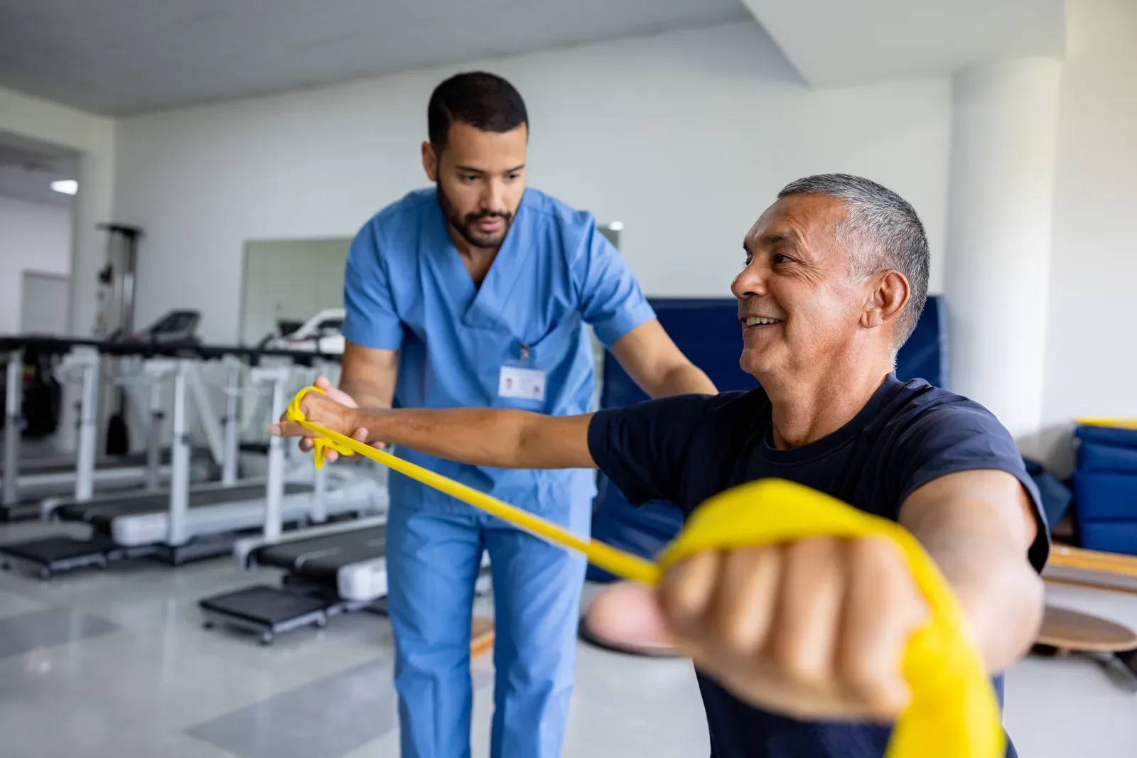 Man stretching a resistance band across his chest during a supervised exercise session