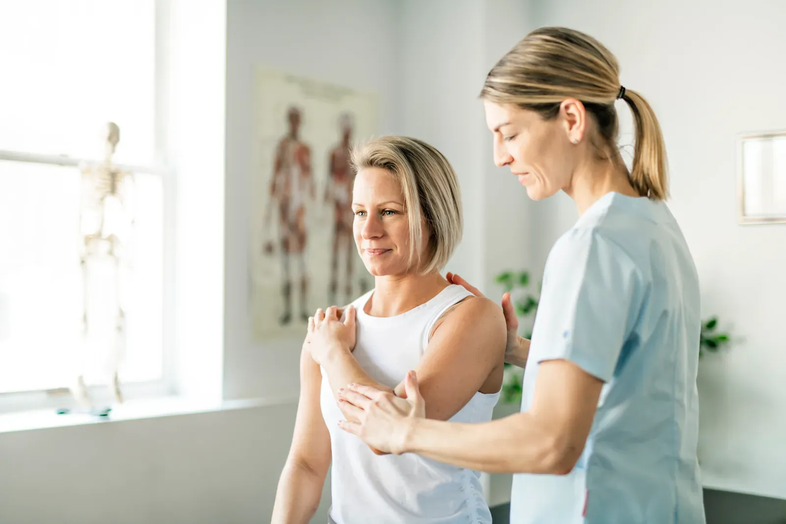 Clinician guiding a woman through a seated exercise in a bright rehabilitation room