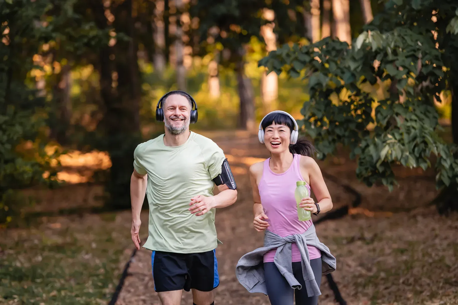Middle-aged couple jogging through a forest at sunset, getting in shape together