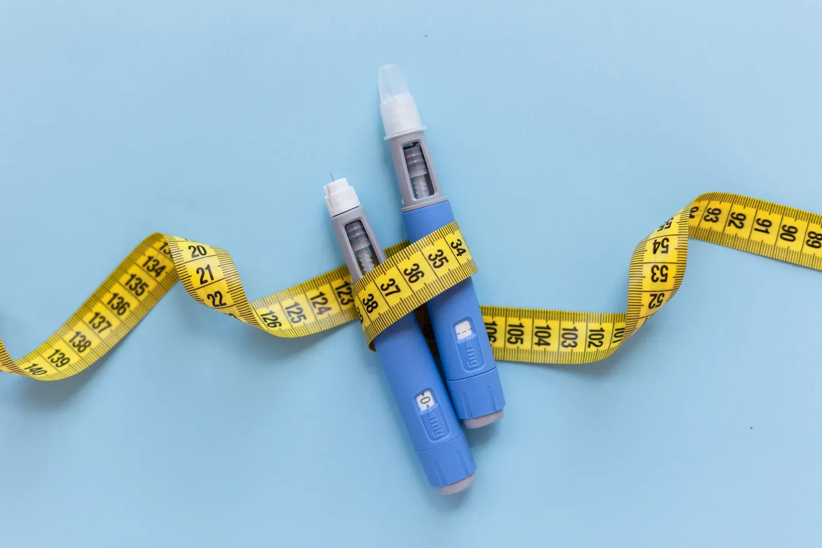 GLP-1 injector pens arranged next to a yellow tape measure on a countertop