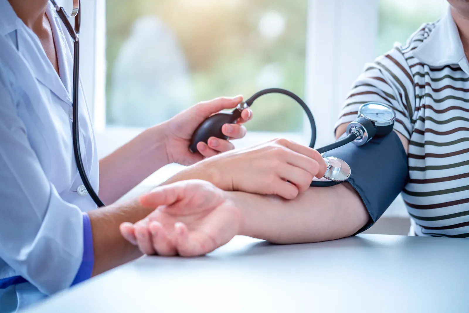 Physician wrapping a blood pressure cuff around a patient's arm in an exam room