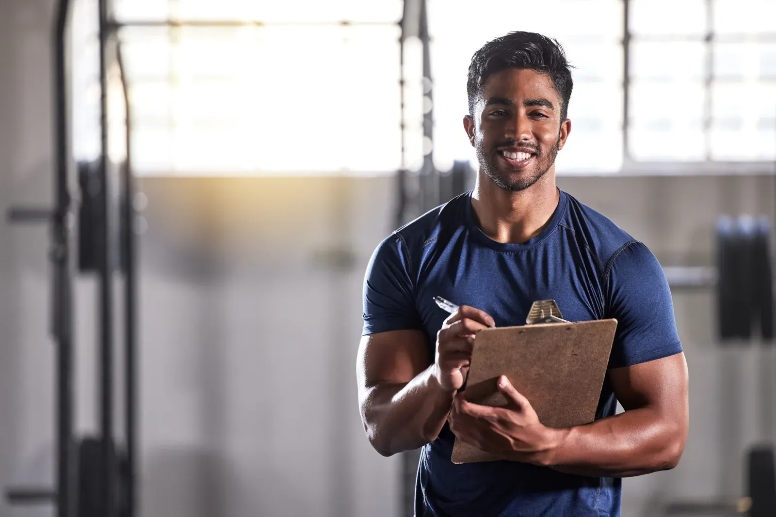 Smiling personal trainer holding a clipboard to log a client's gym progress
