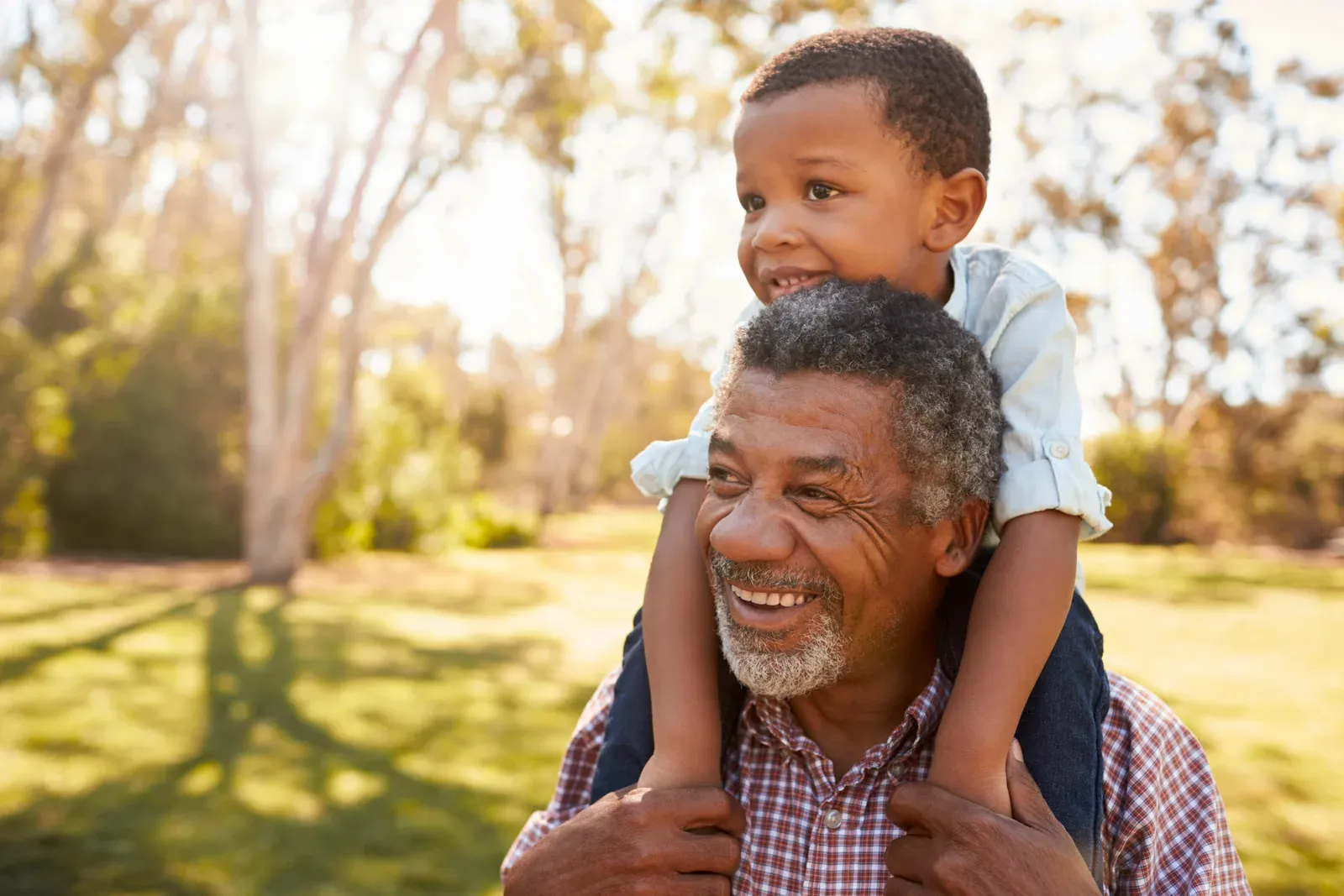 A grandfather carrying his grandson on his shoulders during a walk in the park