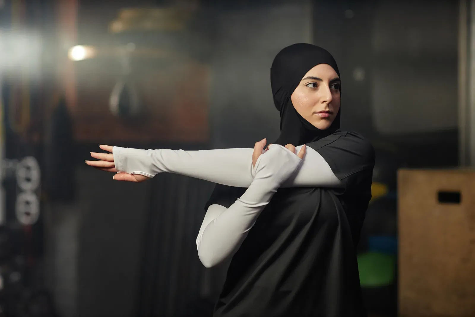 A young woman in a hijab and activewear stretching her arm before a workout