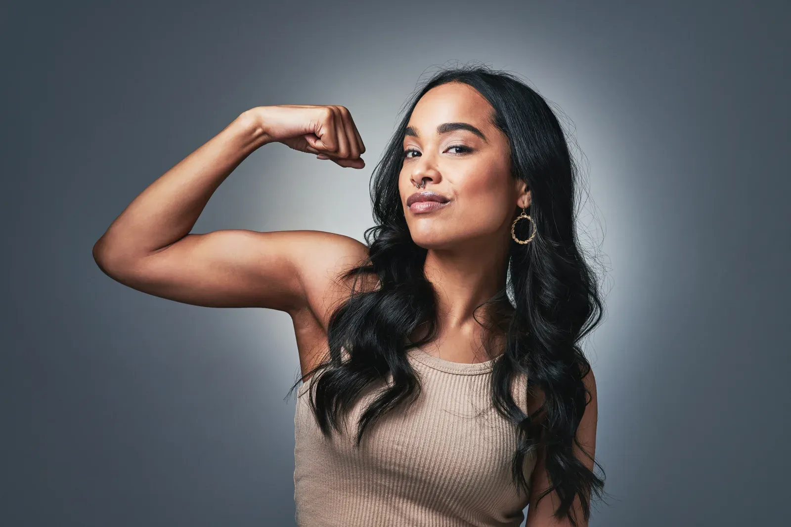 A young woman flexing both arms against a plain grey backdrop