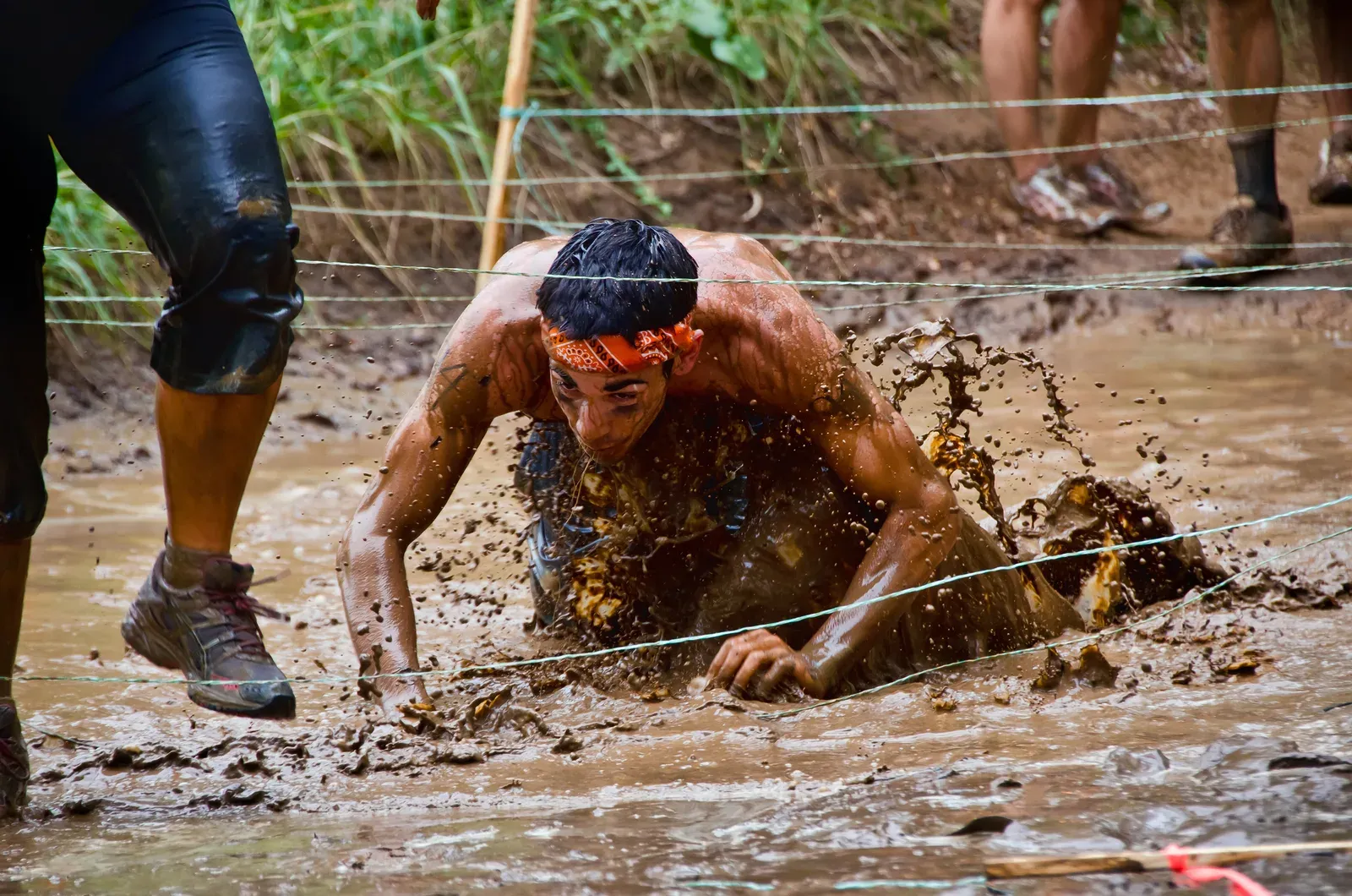 An obstacle race participant crawling through mud under low wires