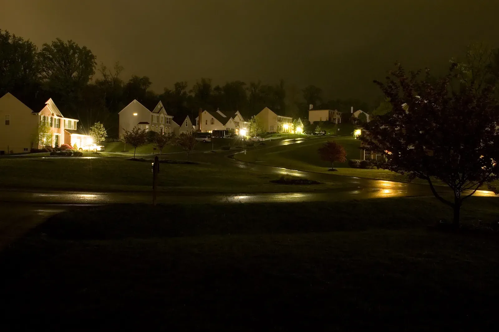 Suburban homes with porch lights glowing along a wet evening street