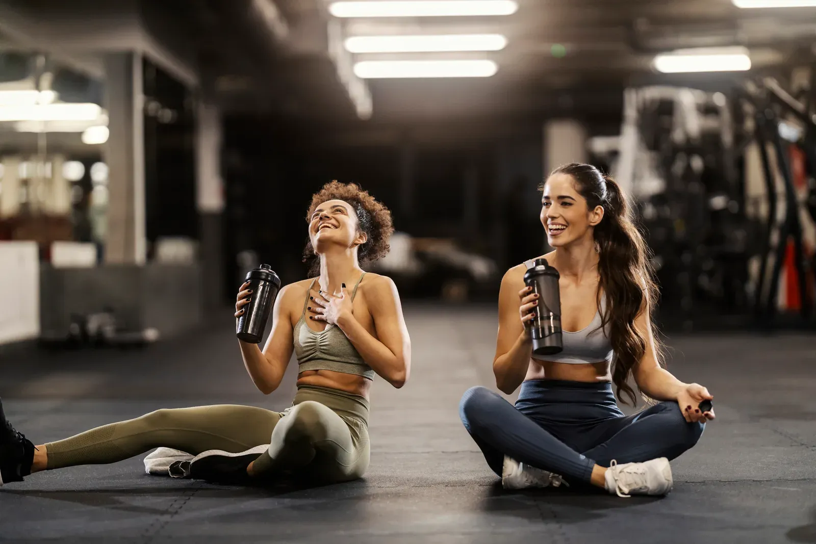Two friends drinking water on the gym floor during a post workout break