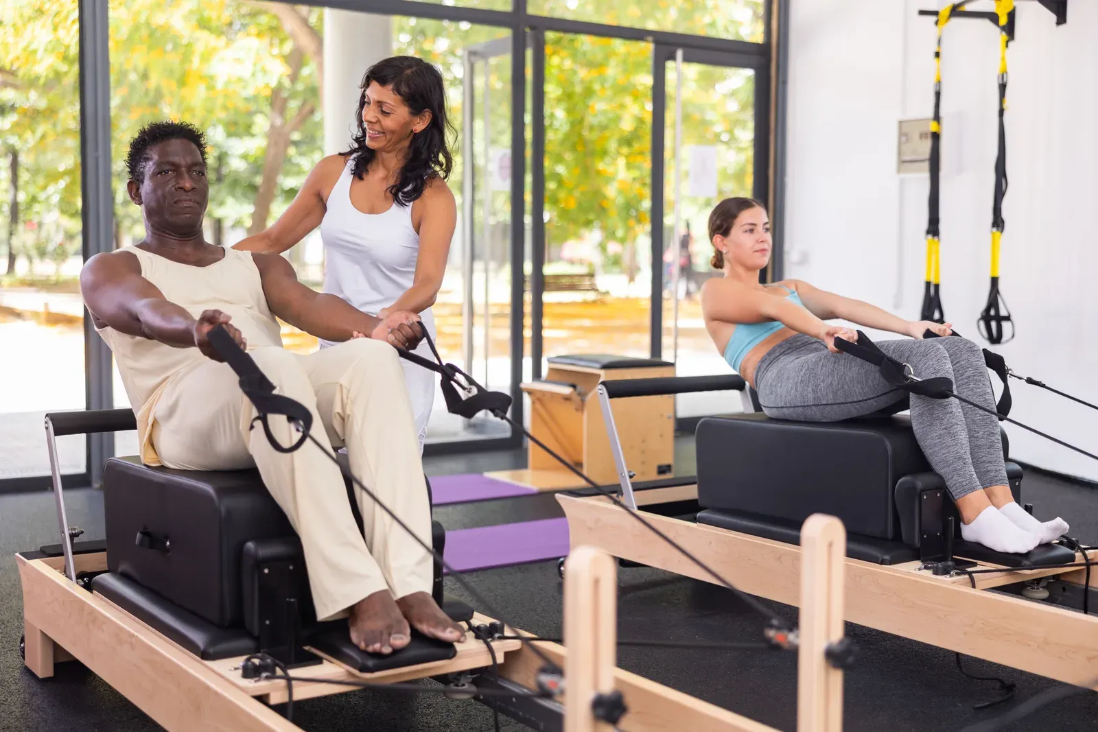 An instructor guiding a woman through slow, controlled floor work in a quiet studio