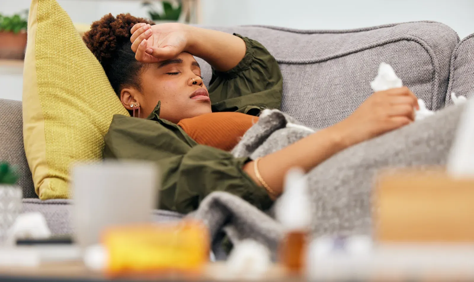Woman resting on the sofa with tissues while fighting a cold or flu