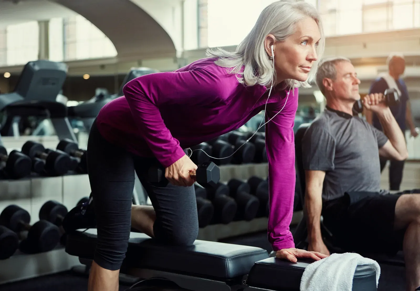 Confident mature woman lifting a dumbbell on a gym bench, strong after 50