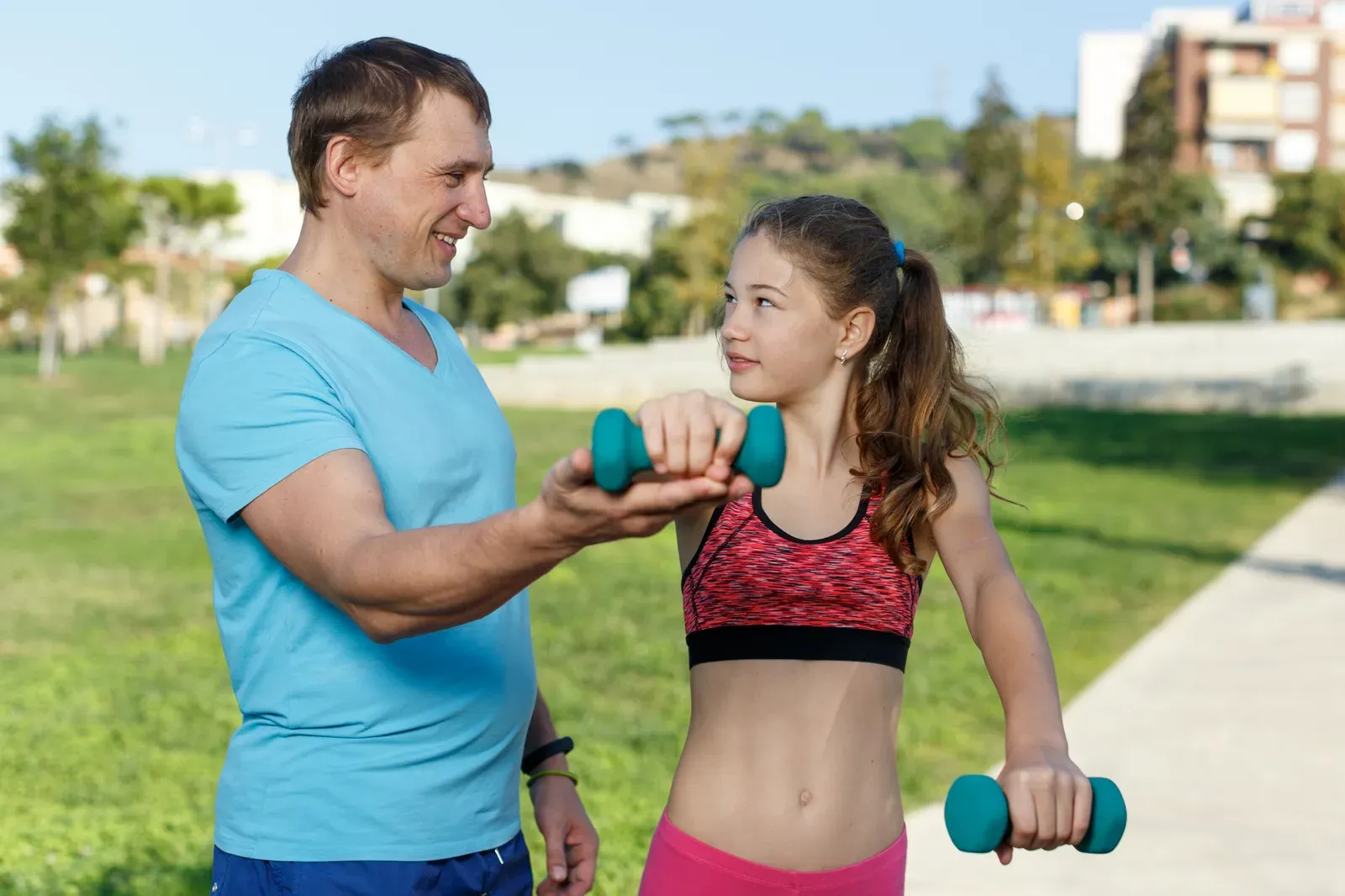 A girl exercising with light dumbbells alongside her father