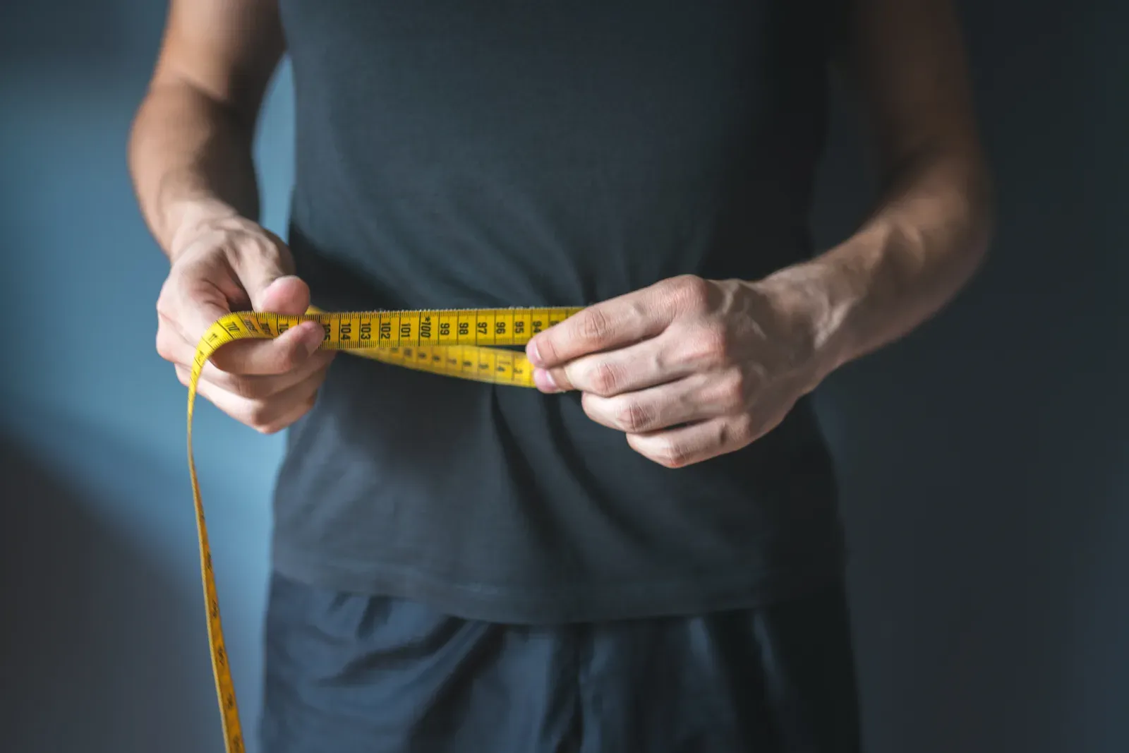 A lean man wrapping a tape measure around his waist